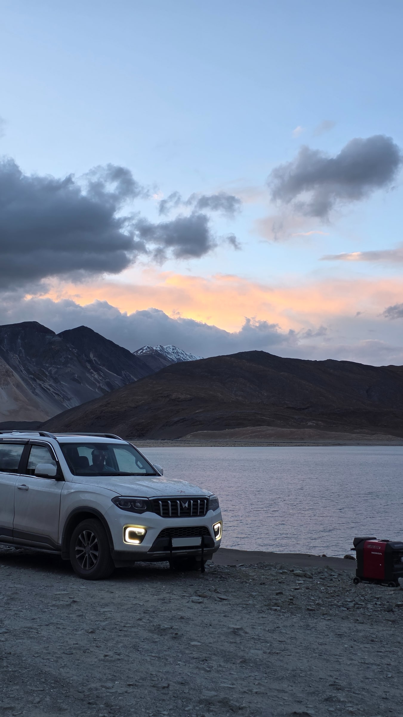 A vehicle on the Pangong shore at dusk with the lake and mountains beyond